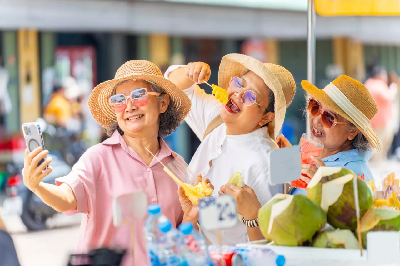 Group of Happy Asian senior woman enjoy travel in the city on summer holiday vacation. Elderly women friends using smartphone taking selfie during travel street market and eating street food together.
